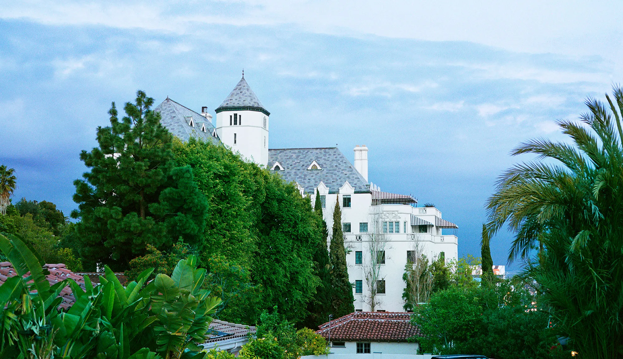 Pale rendered building with steep roofs standing on a slope above a road