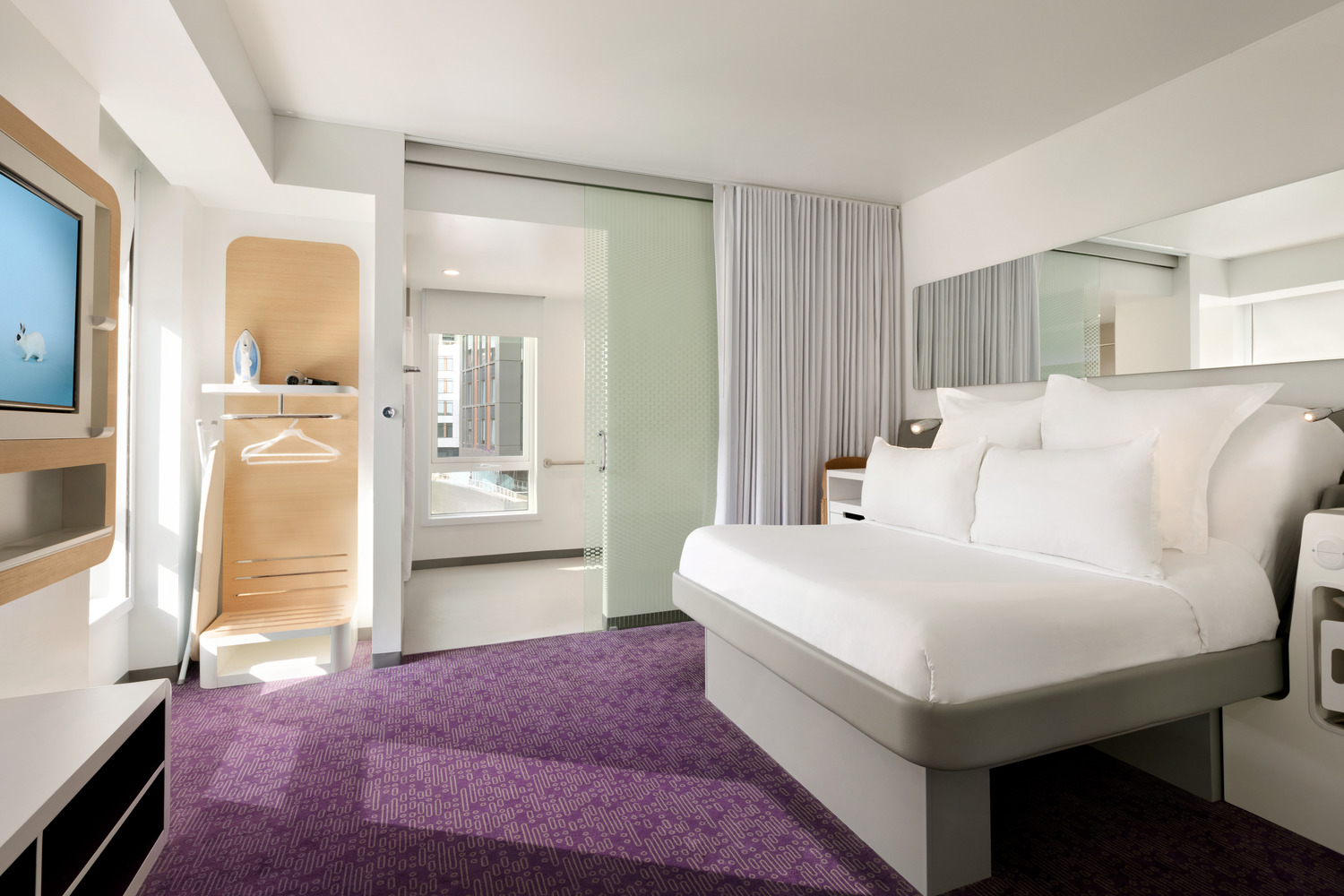 Compact hotel room with a wall-width bed, a window and a narrow work surface